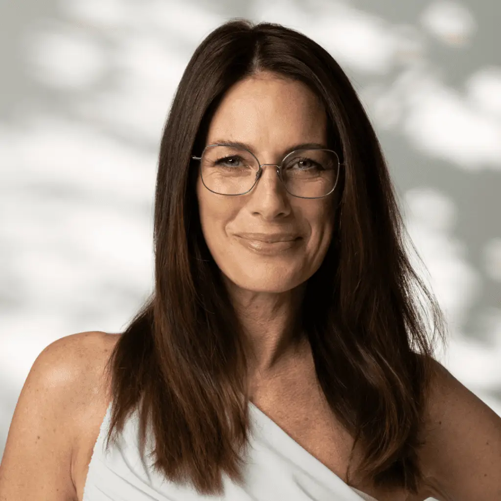 Lächelnde Frau mit Colibris Brille und weißem Oberteil.