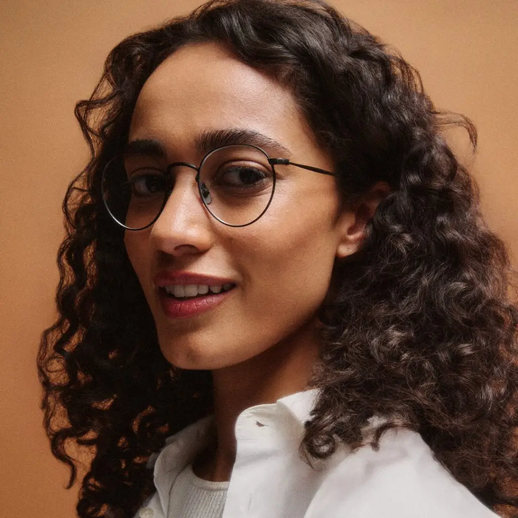 Frau mit GLCO Brille Wilson und lockigen Haaren lächelt.