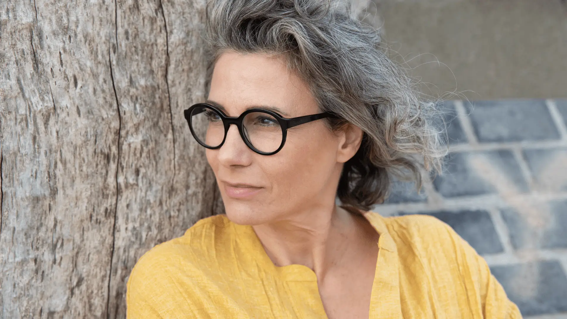 Frau mit Brille von Hamburg Eyewear lehnt an Baum.