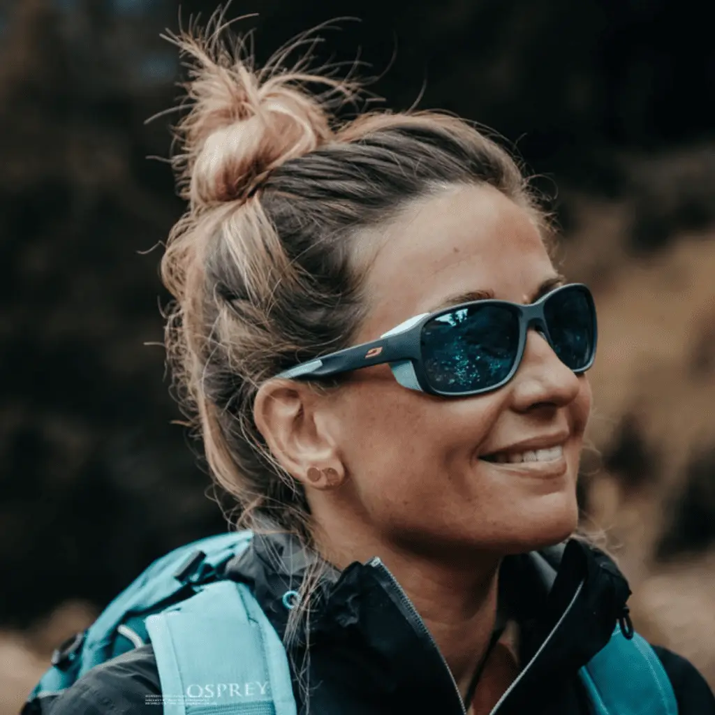Frau mit Sonnenbrille Monterosa von Julbo und Rucksack lächelt outdoors.